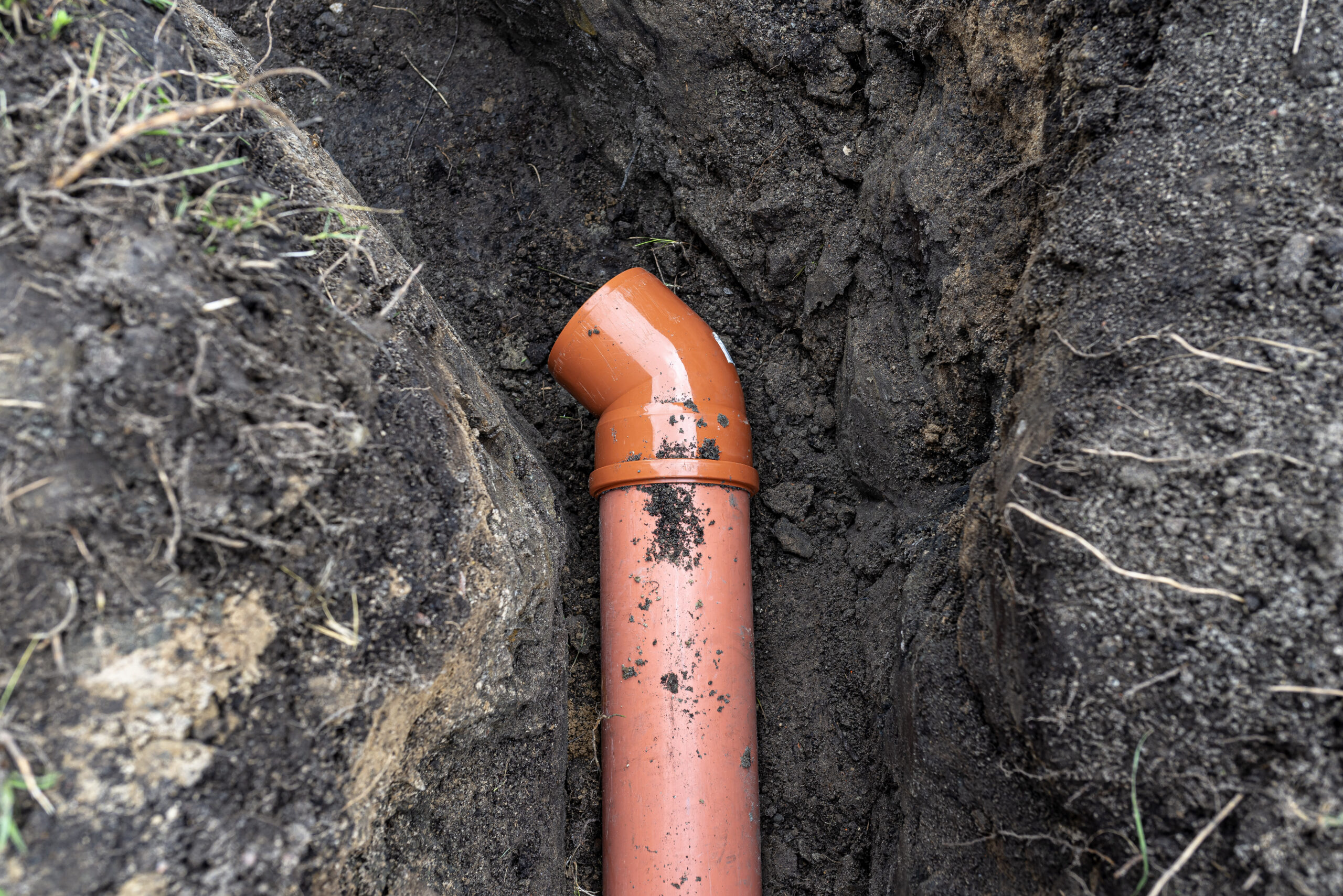 An orange plastic pipe from a septic tank with a diameter of 160 mm lying in a ditch.