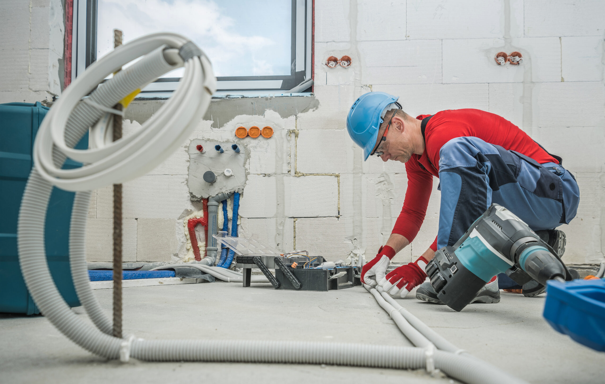 Caucasian Professional Electrician at Work. Electric Cables Plastic Pipe Conduit Installation Inside Newly Constructed House.